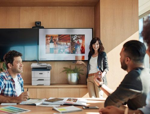 Smiling work team in front of a screen next to a Xerox® B305 multifunction printer