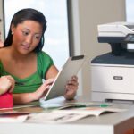 Two women using a tablet in front of a Xerox® VersaLink® B415 Multifunction Printer