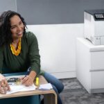 Smiling woman in an office next to the Xerox® VersaLink® C620 Colour Printer